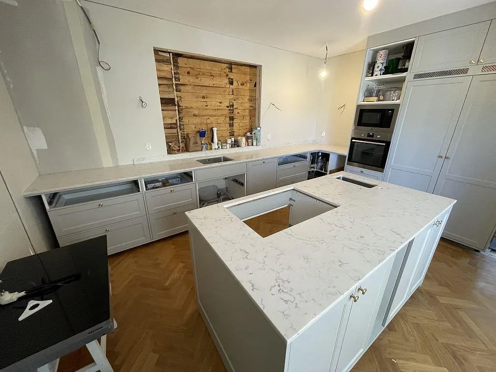 Polerad köksö i Technistone Mystery White med hällurtag och liten rostfri ho framför en väggbänk i samma sten i Österskär.