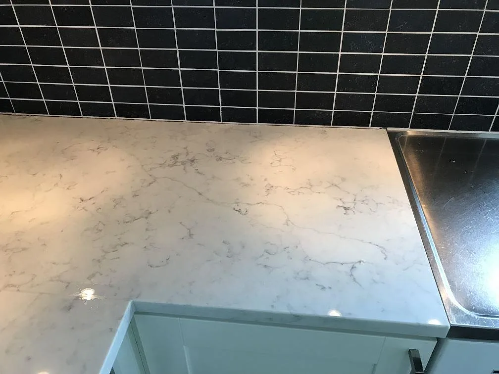 Vit Technistone Mystery White bänkskiva med rostfri diskho och svart kakelstänkskydd i ett kök i Rydebäck.