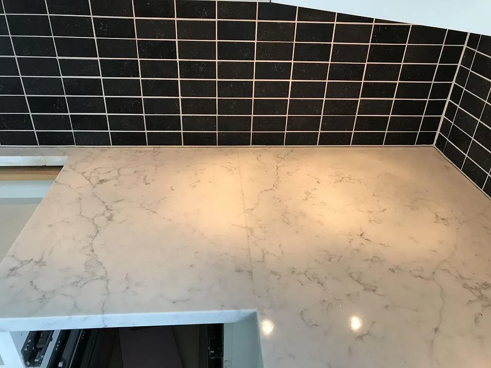 Hörnparti av polerad Technistone Mystery White bänkskiva med grå ådring som speglar takbelysningen i ett kök i Rydebäck.