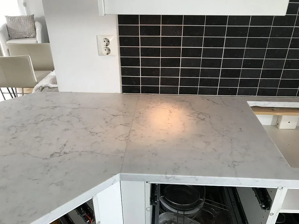 Detalj av vit Technistone Mystery White köksbänkskiva med mjuk grå ådring mot svart kakel i Rydebäck.