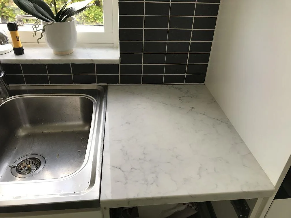 Bänkskiva i vit Technistone Mystery White med underlimmad rostfri diskho vid fönstret i ett kök i Rydebäck.