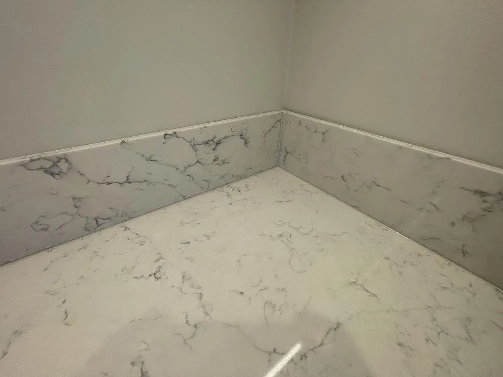 Polerad bänkskiva i vit Technistone Mystery White med grå ådring och uppvikt stänkskydd i samma kvartskomposit i ett kök i Saltsjöbaden.