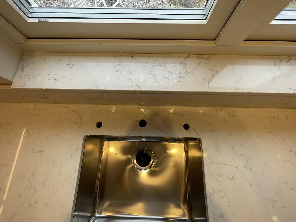 Underlimmad rostfri diskho och fönsterbänk i vit Technistone Mystery White kvartskomposit med grå ådring och borrade blandarhål i ett kök i Saltsjöbaden.