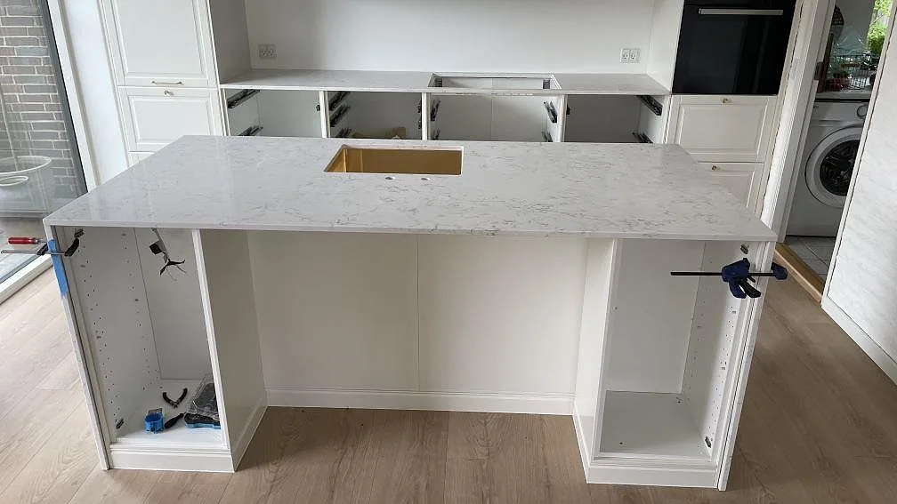 Köksö med köksbänkskiva i polerad Technistone Mystery White, vit kvartskomposit med grå ådring och synlig diskho, under montering i Solrød.