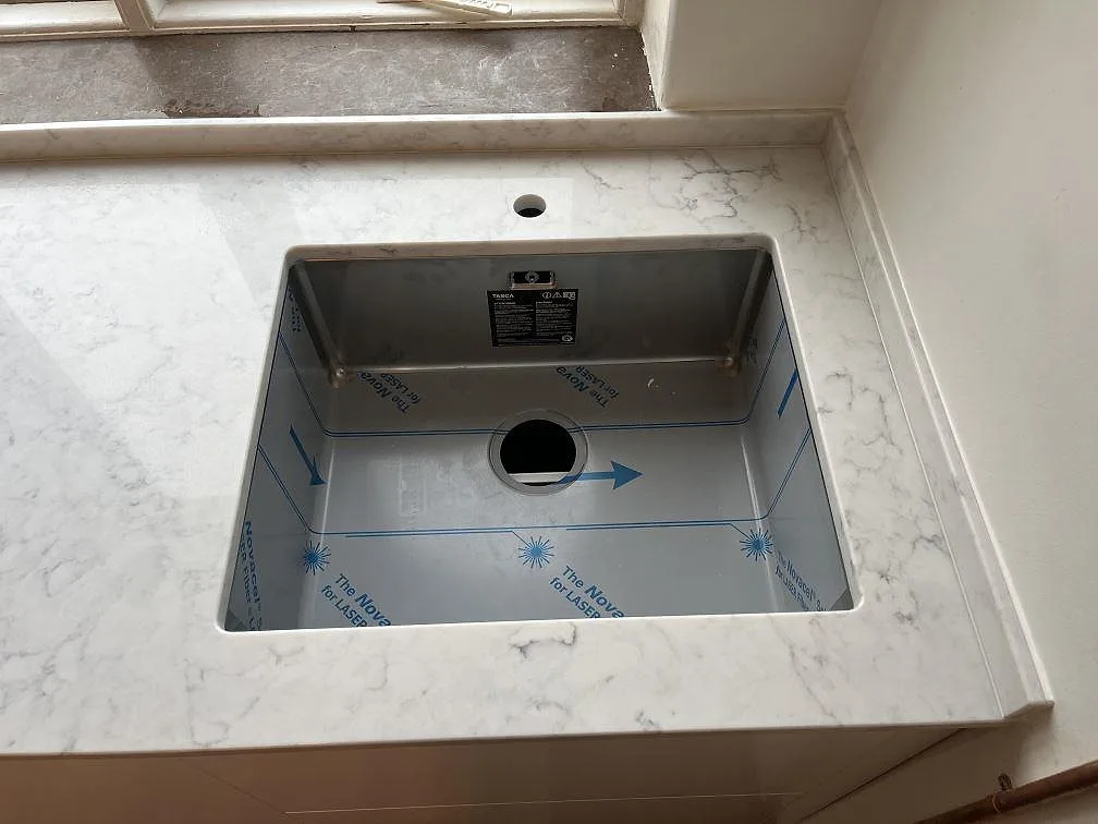 Underlimmad rostfri diskho i polerad Technistone Mystery White kompositbänkskiva vid ett fönster i Stockholm.