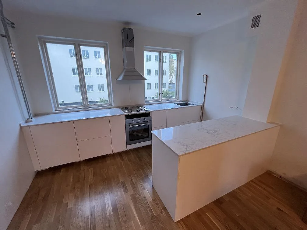 Köksbänkskiva i vit Technistone Mystery White komposit, polerad, med halvö, diskho och gashäll i ett kök i Stockholm.