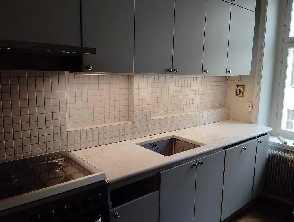 Polerad köksbänkskiva i vit Technistone Mystery White komposit med öppning för underlimmad diskho, grå luckor och mosaikkakel i Stockholm.