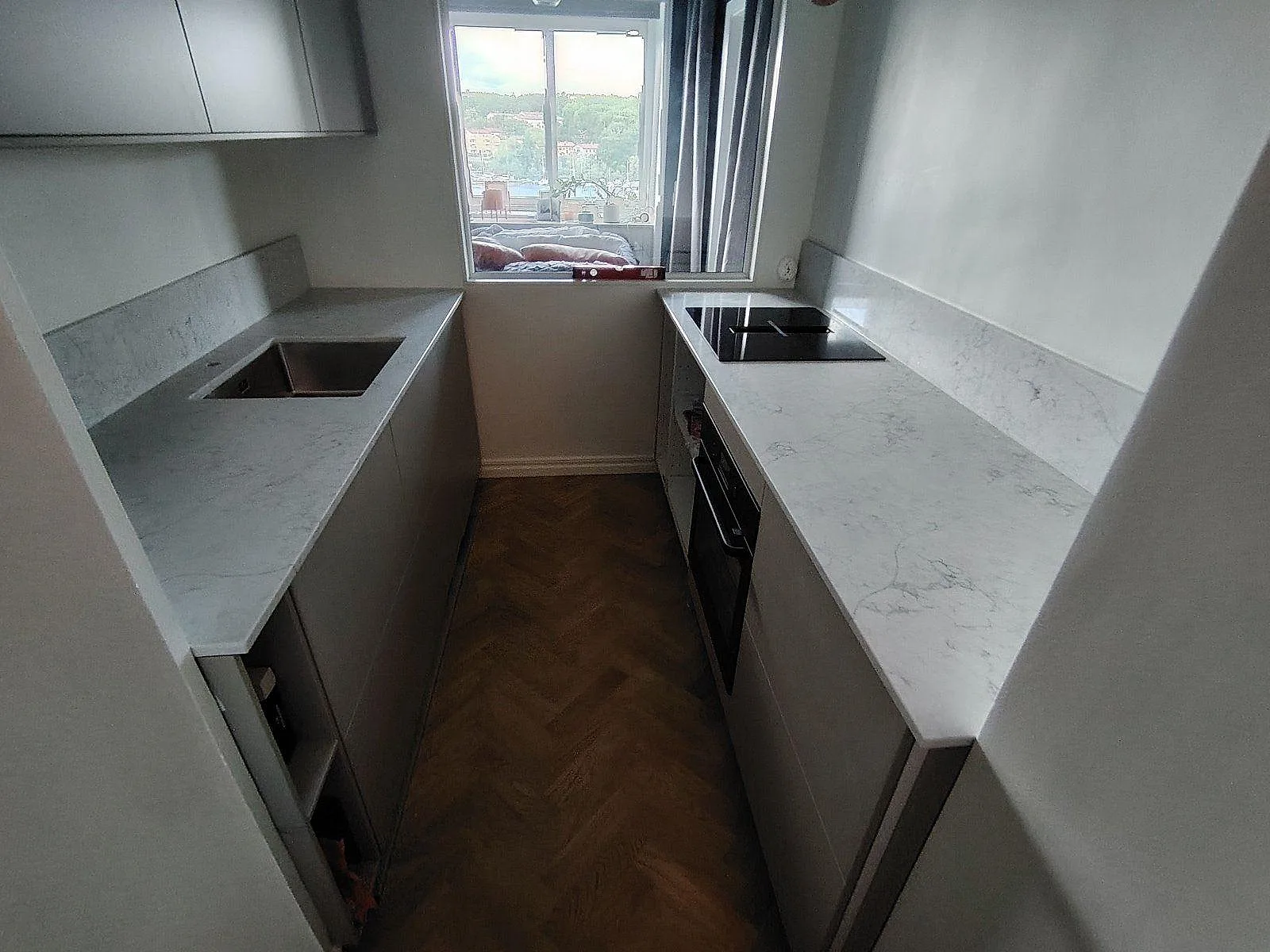 Köksbänkskiva i Technistone Mystery White komposit, polerad, med svart induktionshäll och låg stänkkant i ett kompakt kök i Stockholm.