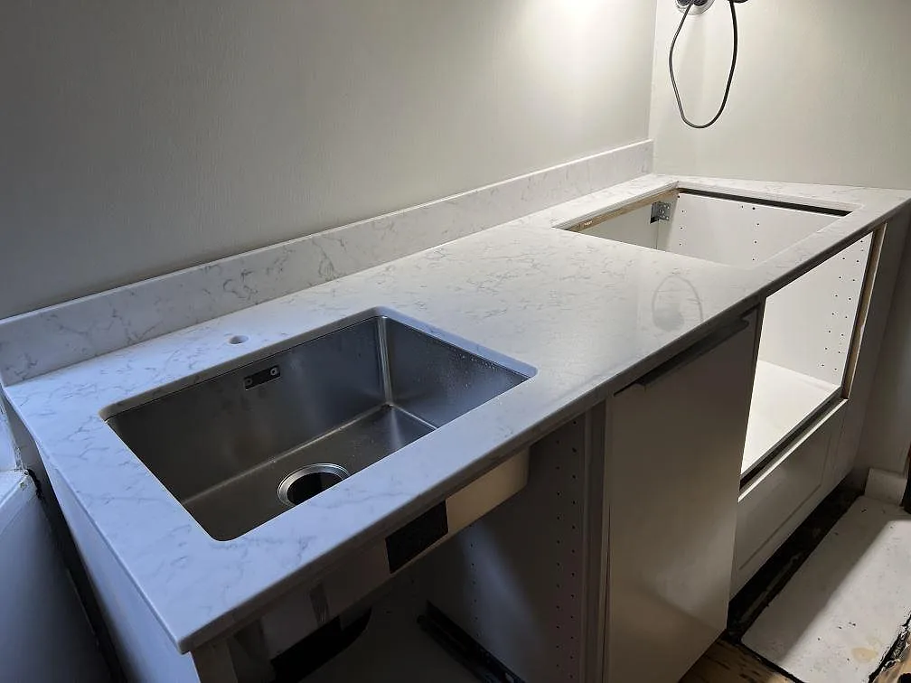 Närbild på polerad köksbänkskiva i Technistone Mystery White med underlimmad rostfri diskho, blandarhål och grå ådring i Stockholm.