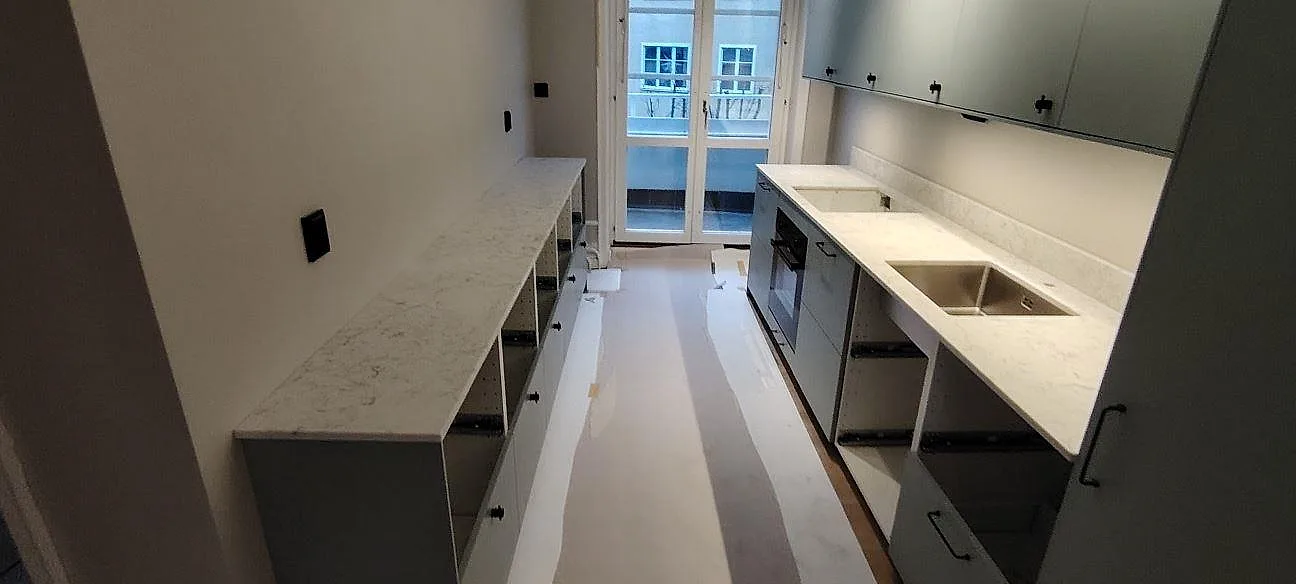 Vitt kök under montering i Stockholm med bänkskivor i polerad Technistone Mystery White komposit på två sidor.