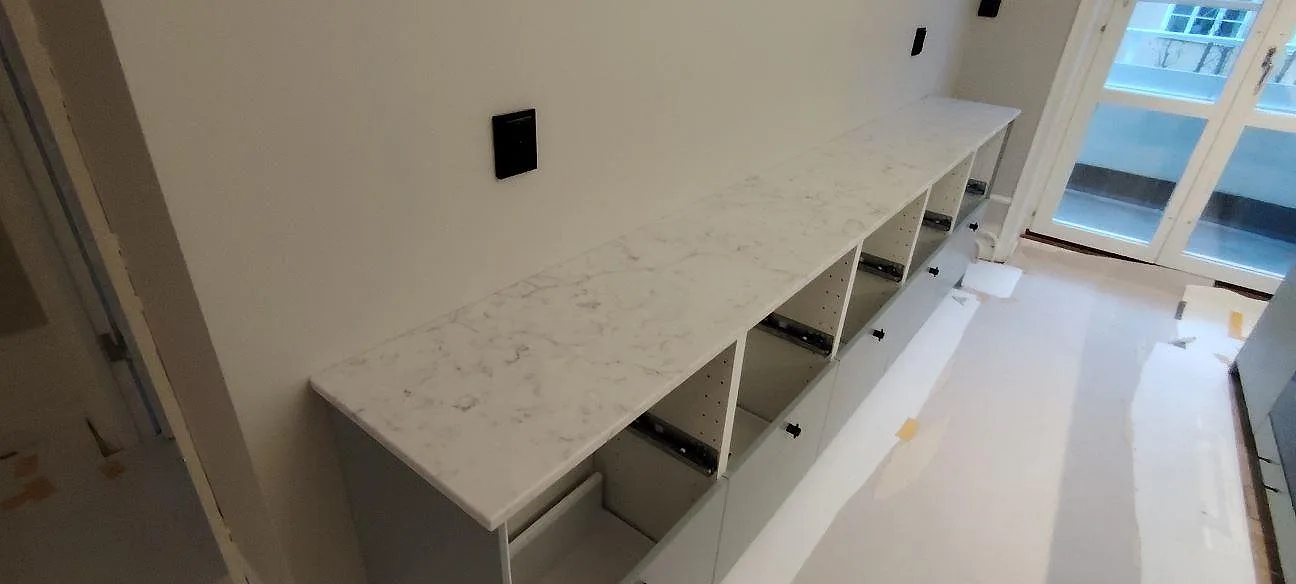 Sidobänk i polerad Technistone Mystery White komposit med ljus ådring och öppna köksstommar i Stockholm.