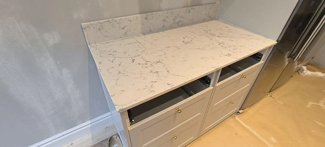Detalj av vänster köksbänk i Stockholm med polerad Technistone Mystery White komposit, grå ådring och uppvikt stänkkant.