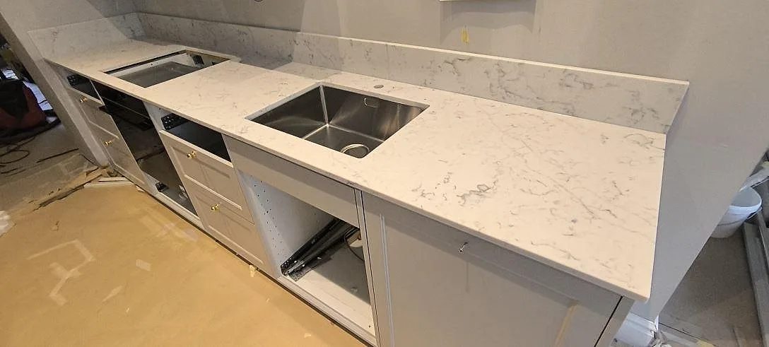 Närbild av köksbänkskiva i polerad Technistone Mystery White komposit med rostfri diskho, hällöppning och grå ådring i Stockholm.