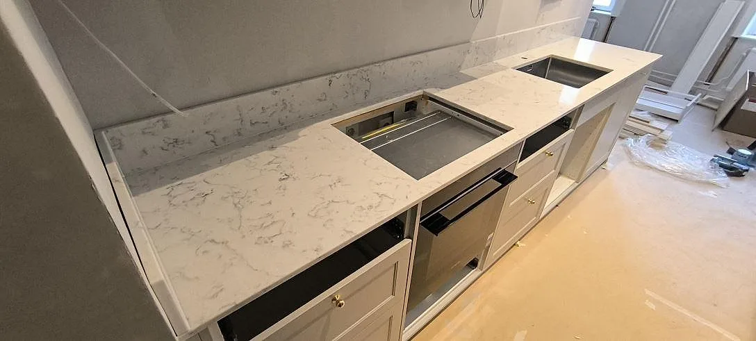 Polerad Technistone Mystery White komposit i ett kök i Stockholm med hällöppning, rostfri diskho och stänkkant längs väggen.