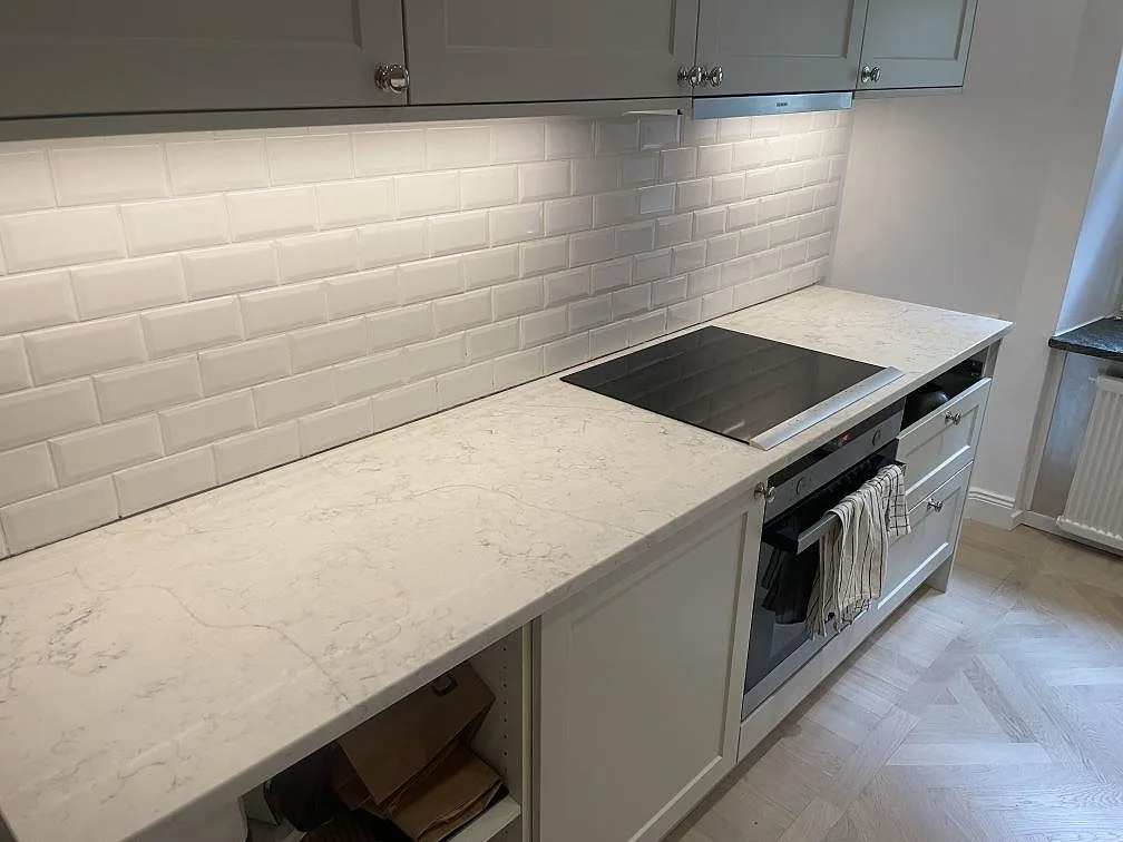 Polerad köksbänkskiva i Technistone Mystery White med häll och vit kakelvägg i ett kök i Stockholm.
