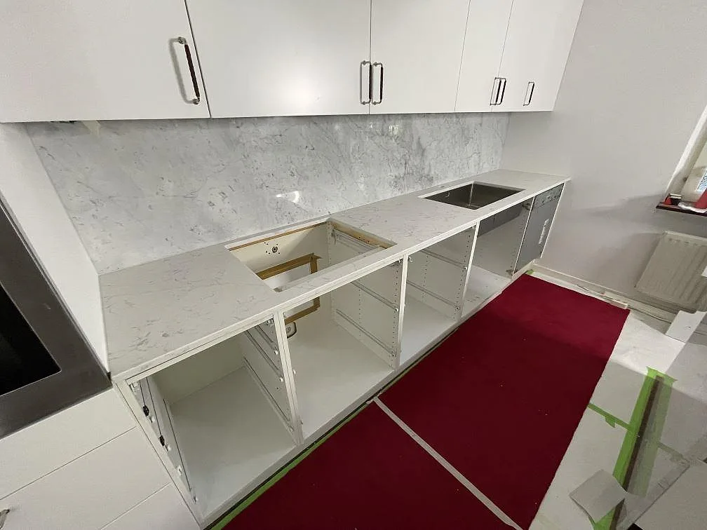 Lång köksbänkskiva i polerad Technistone Mystery White med stenklädd bakyta och öppna köksstommar i Stockholm.