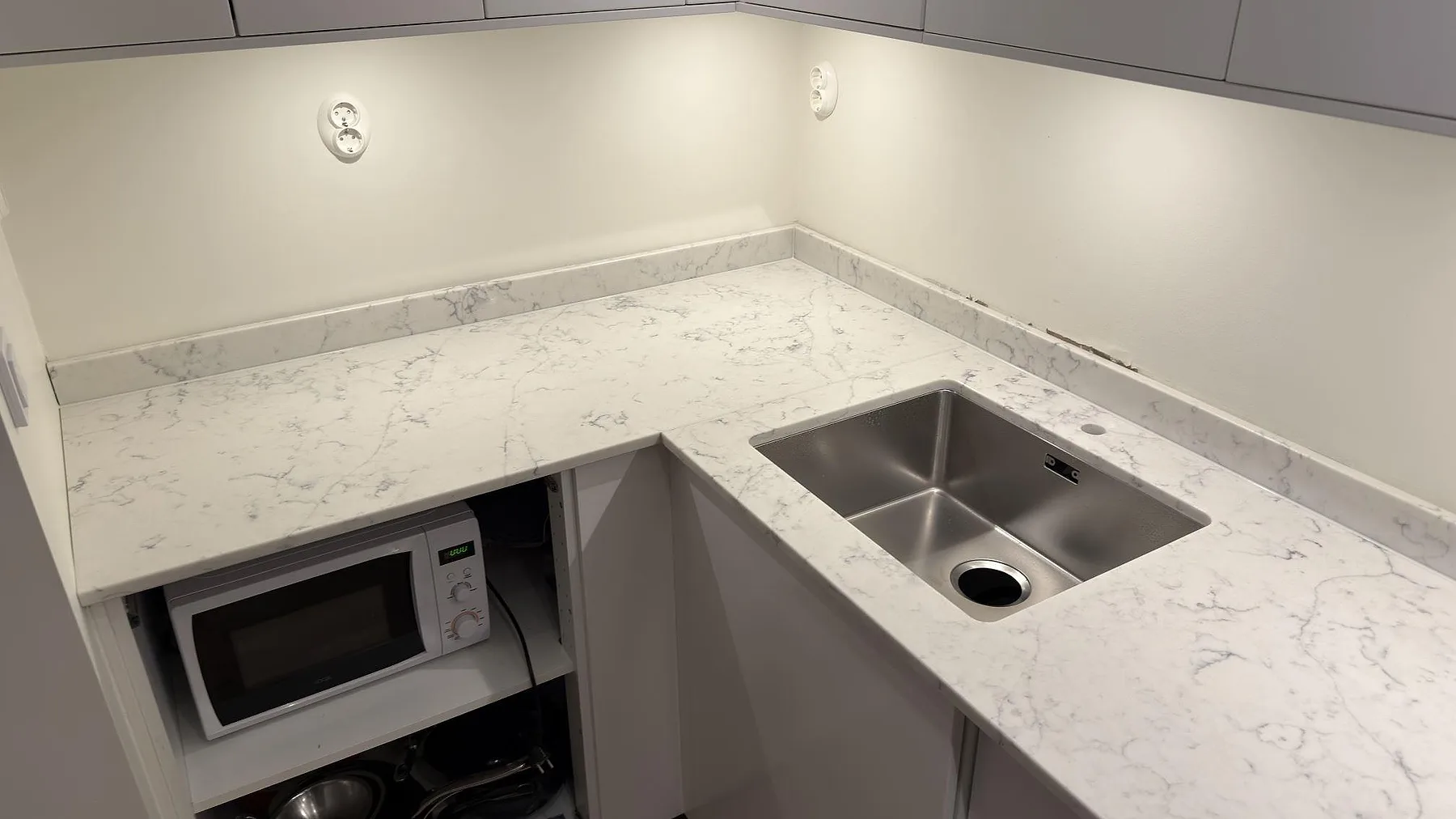 Polerad bänkskiva i Technistone Mystery White med underlimmad rostfri diskho och uppvikt stänkkant i ett kompakt kök i Stockholm.