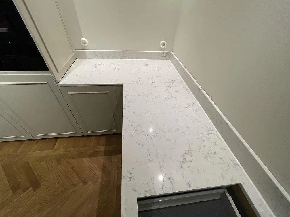 Polerad köksbänkskiva i Technistone Mystery White med grå marmorlik ådring sett ovanifrån längs den L-formade bänken i ett kök i Stockholm.