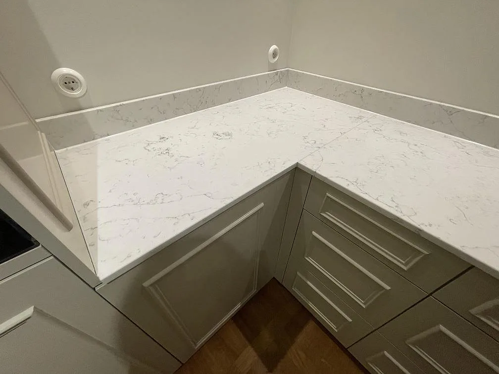 Närbild på hörnet av en köksbänkskiva i Technistone Mystery White med uppvikt stänkkant i samma sten och tydlig grå ådring i ett kök i Stockholm.