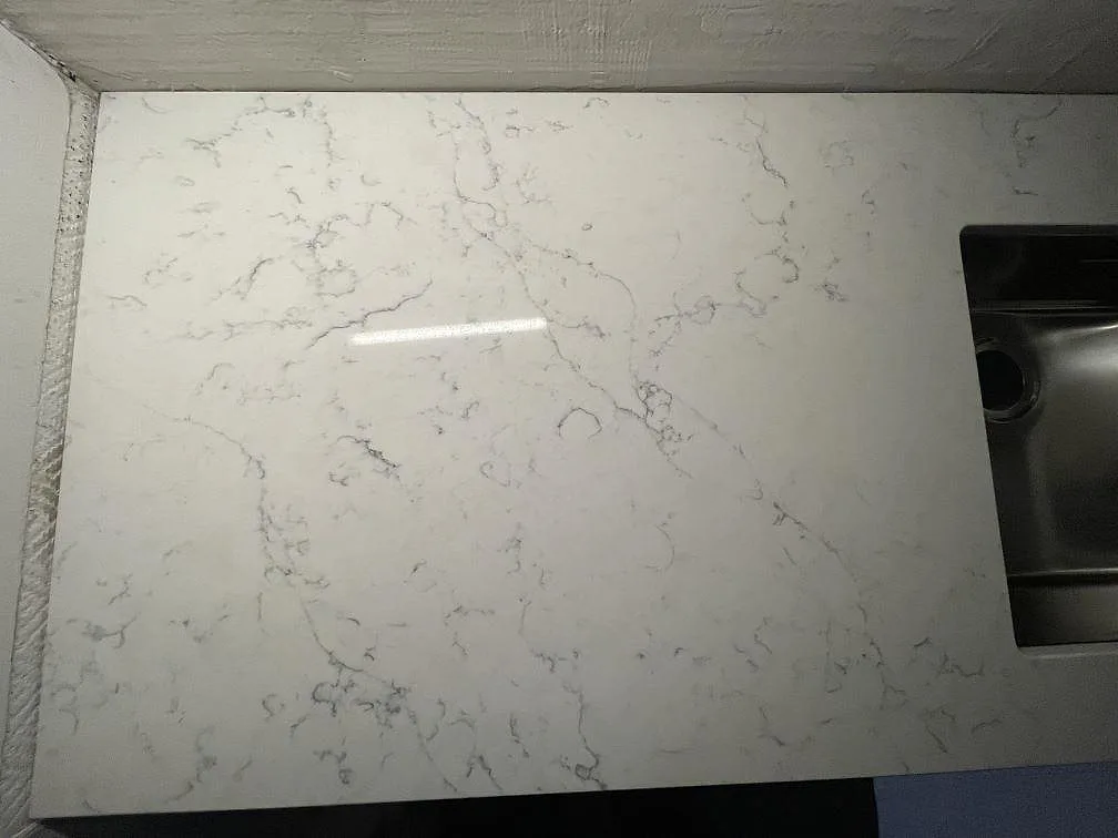 Polerad köksbänkskiva i Technistone Mystery White ovanifrån, med fin marmorlik ådring och en underlimmad rostfri diskho i ett kök i Stockholm.
