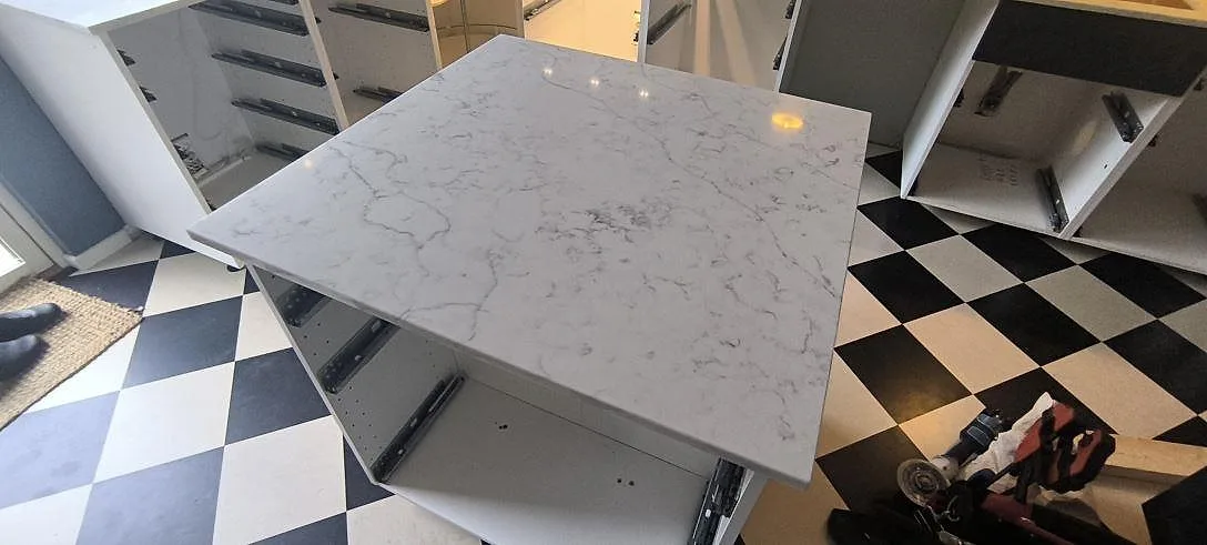 Närbild på köksö i polerad Technistone Mystery White, vit komposit med grå ådring, under montering i Täby.