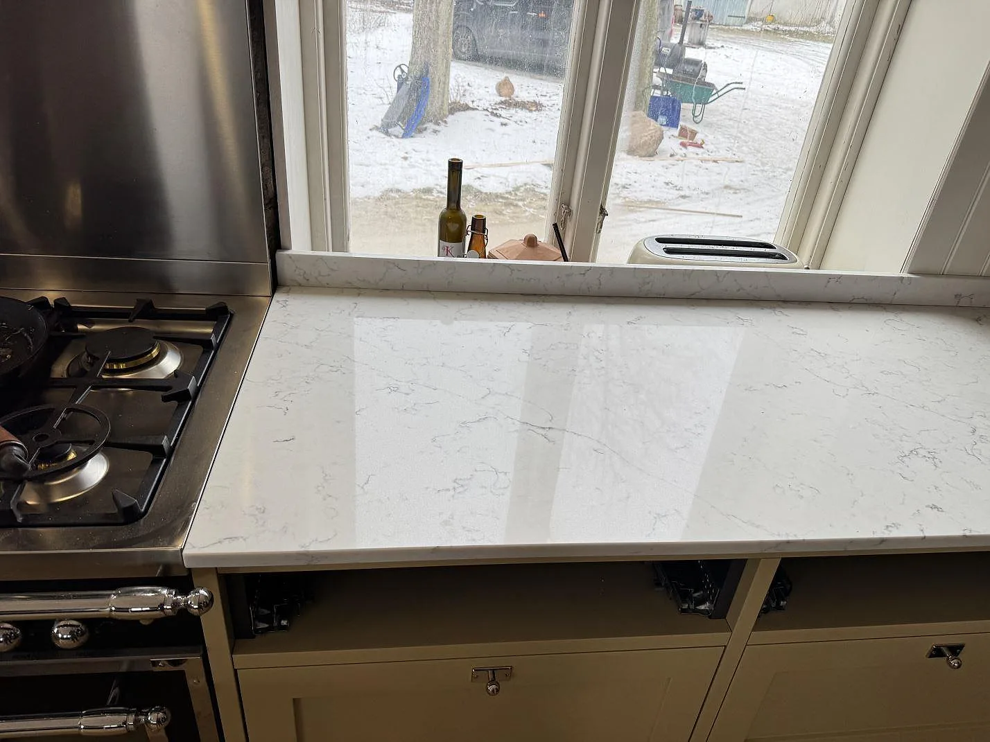 Polerad Technistone Mystery White bänkskiva intill en fristående rostfri spis i ett kök i Tygelsjö, med fönsterbänk i samma sten.