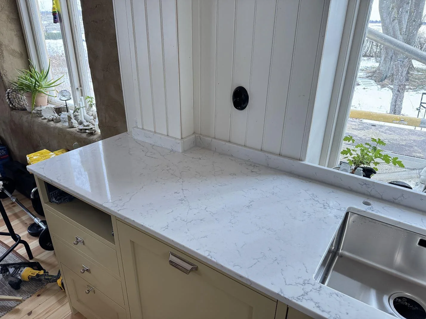 Polerad Technistone Mystery White köksbänkskiva längs väggen med rostfri diskho i ett kök under montering i Tygelsjö.
