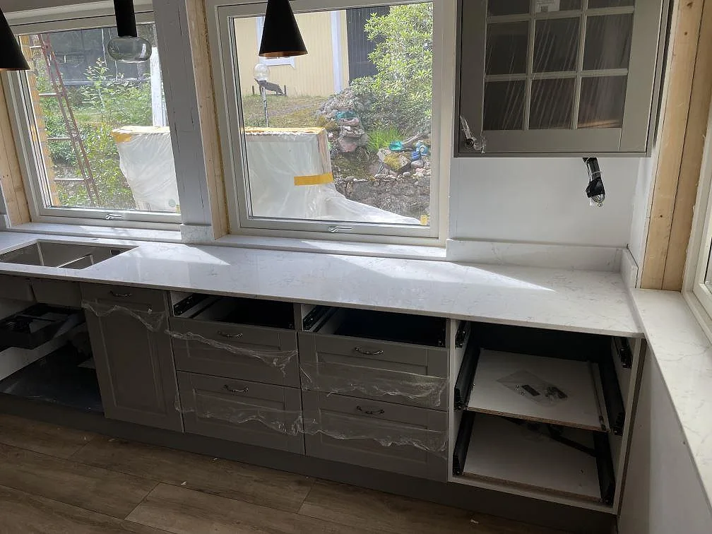 Lång bänkrad under fönster i Tyresö med polerad Technistone Mystery White, låg stänkkant och ljus fönsterbänk i samma komposit.