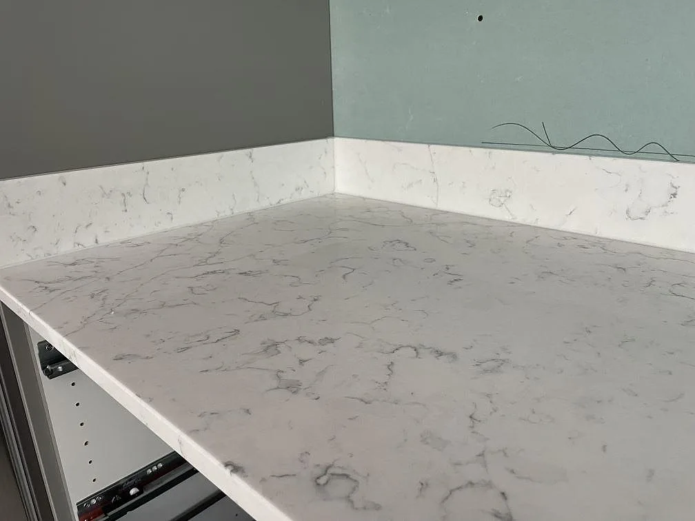 Detalj av vit Technistone Mystery White kvartskomposit med grå ådring, polerad yta och uppvikt stänkkant i ett kök i Tyresö.