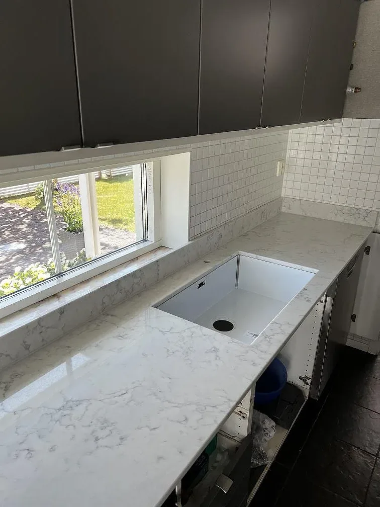 Polerad köksbänkskiva i Technistone Mystery White med diskhozonsöppning och stora fönster i ett kök i Uddevalla.