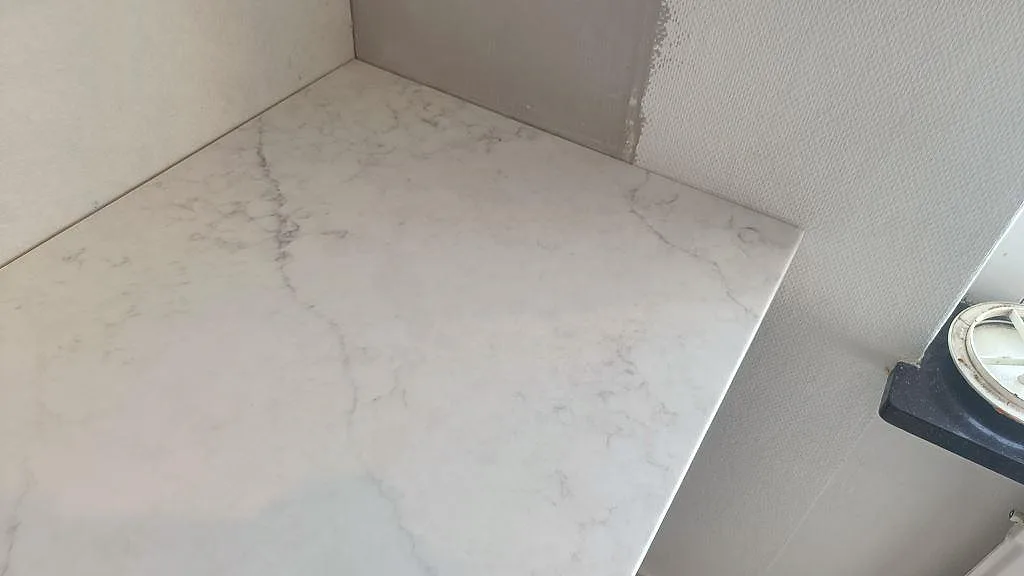 Hörndetalj av polerad Technistone Mystery White kompositbänkskiva med ljus marmorering vid fönster i Västra Frölunda.