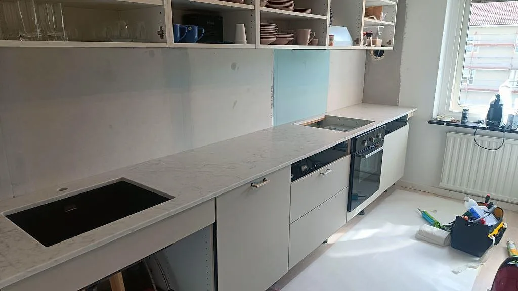 L-formad köksbänkskiva i polerad Technistone Mystery White komposit med svart diskho, häll och ljusblå stänkpanel i Västra Frölunda.