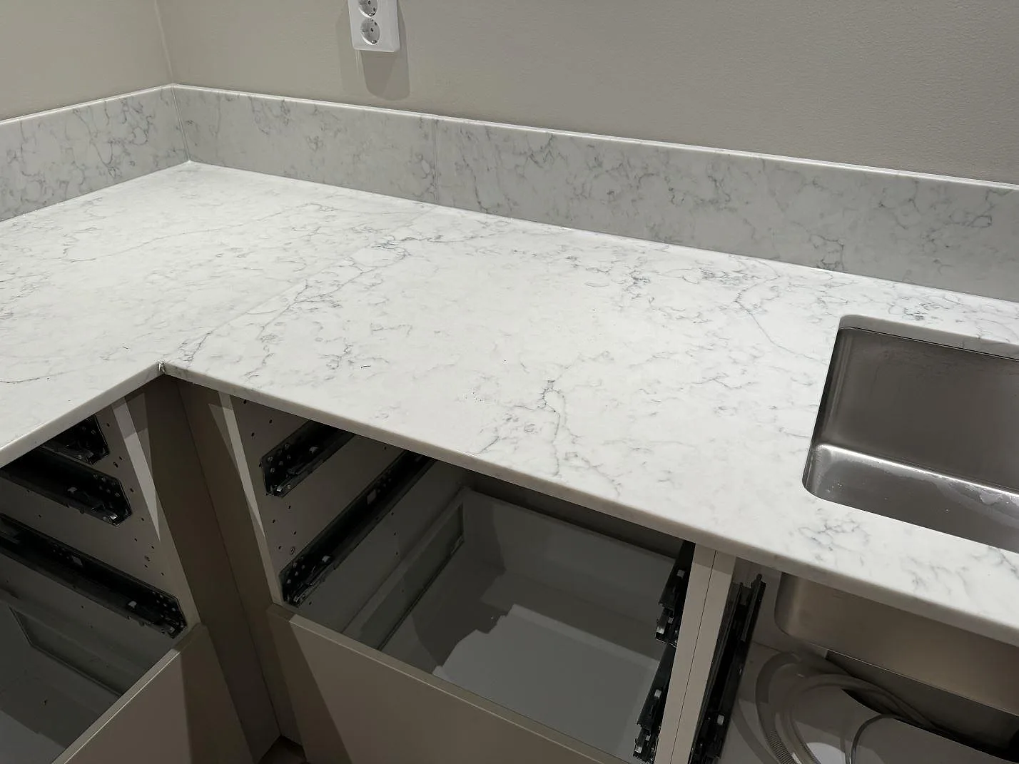 L-formad köksbänkskiva i vit Technistone Mystery White med grå ådring och underlimmad rostfri diskho under montering i Ystad.