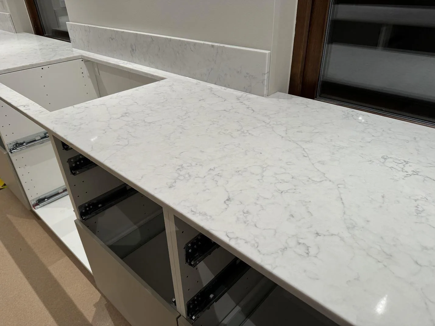 Installerad köksbänkskiva i vit Technistone Mystery White med uppvikt stänkkant och öppna stommar under montering i Ystad.