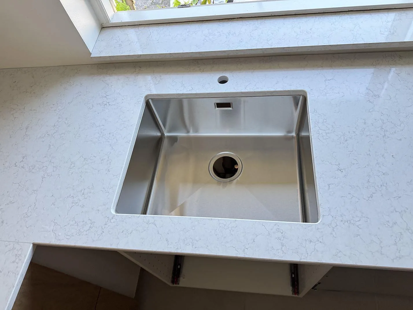 Närbild på rostfri diskho i polerad Technistone Noble Arco komposit med grå ådring i kök i Greve.