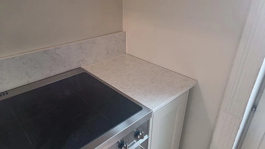 Höger arbetsyta vid fristående spis med Technistone Noble Arco, polerad ljus kvartskomposit och uppvikt stänkkant i Malmö.