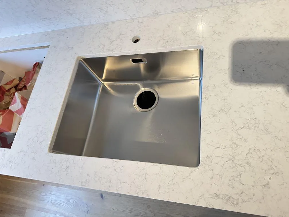Närbild av rostfri diskho monterad under en polerad Technistone Noble Arco bänkskiva med ljus grå ådring i Malmö.