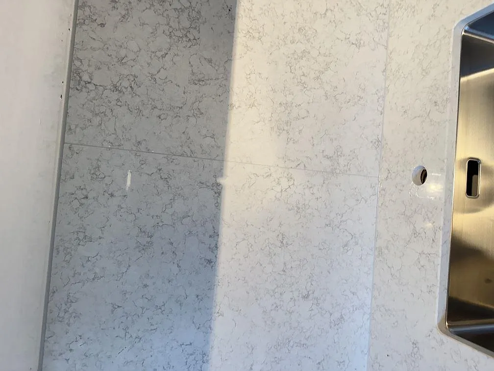 Detaljbild av matchande stänkskydd och bänkskiva i Technistone Noble Arco med rostfri diskho vid kanten i Malmö.