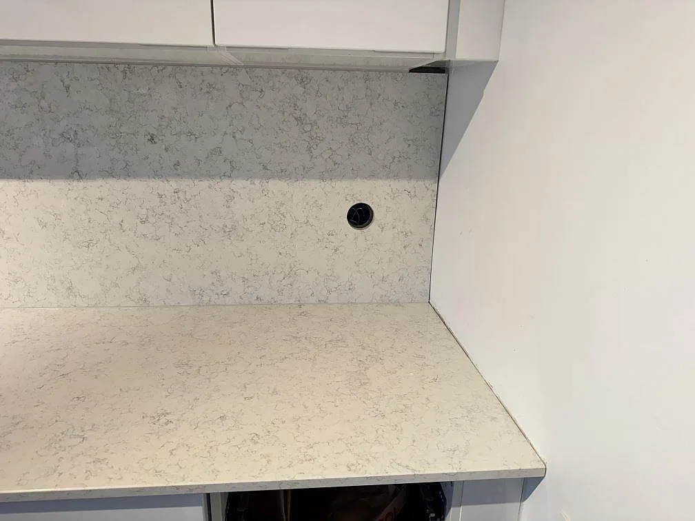 Hörndetalj av köksbänkskiva och stänkskydd i polerad Technistone Noble Arco komposit under överskåp i Malmö.