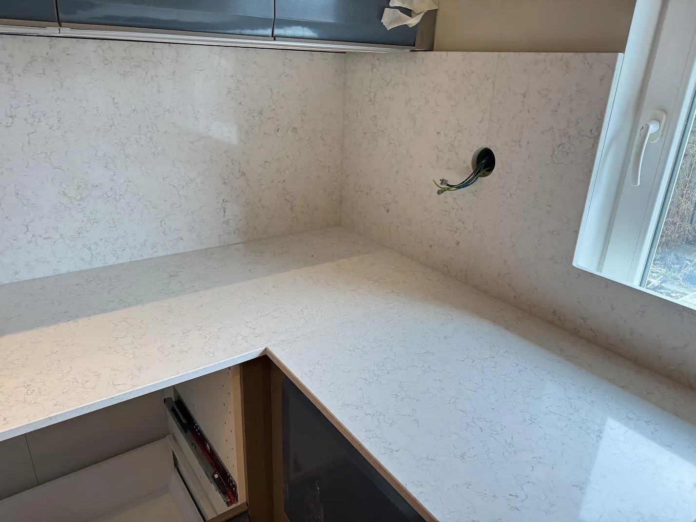 Hörnvy över ljus köksbänkskiva och väggyta i polerad Technistone Noble Arco bredvid fönster i Oxie.