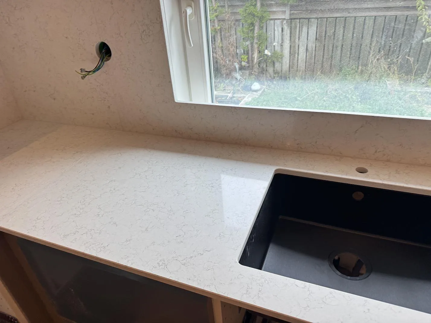Bänkskiva i polerad Technistone Noble Arco vid fönster med svart diskho och ljus kompositsten på väggen, Oxie.