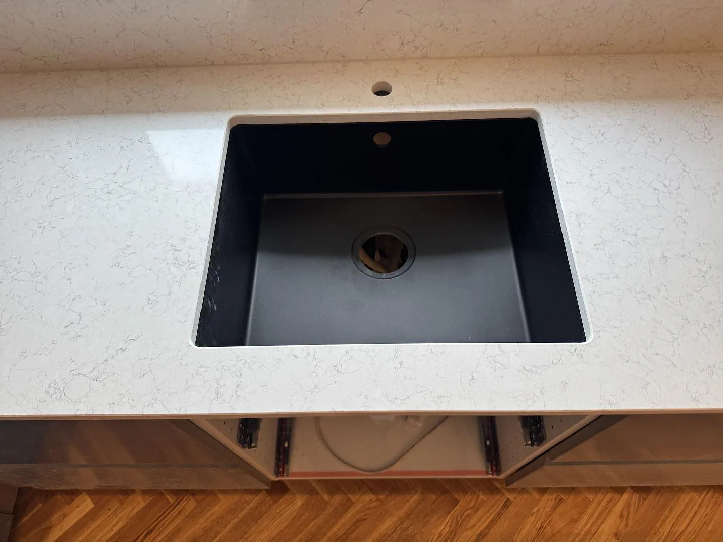 Närbild på svart diskho i köksbänkskiva av polerad Technistone Noble Arco med grå ådring, Oxie.