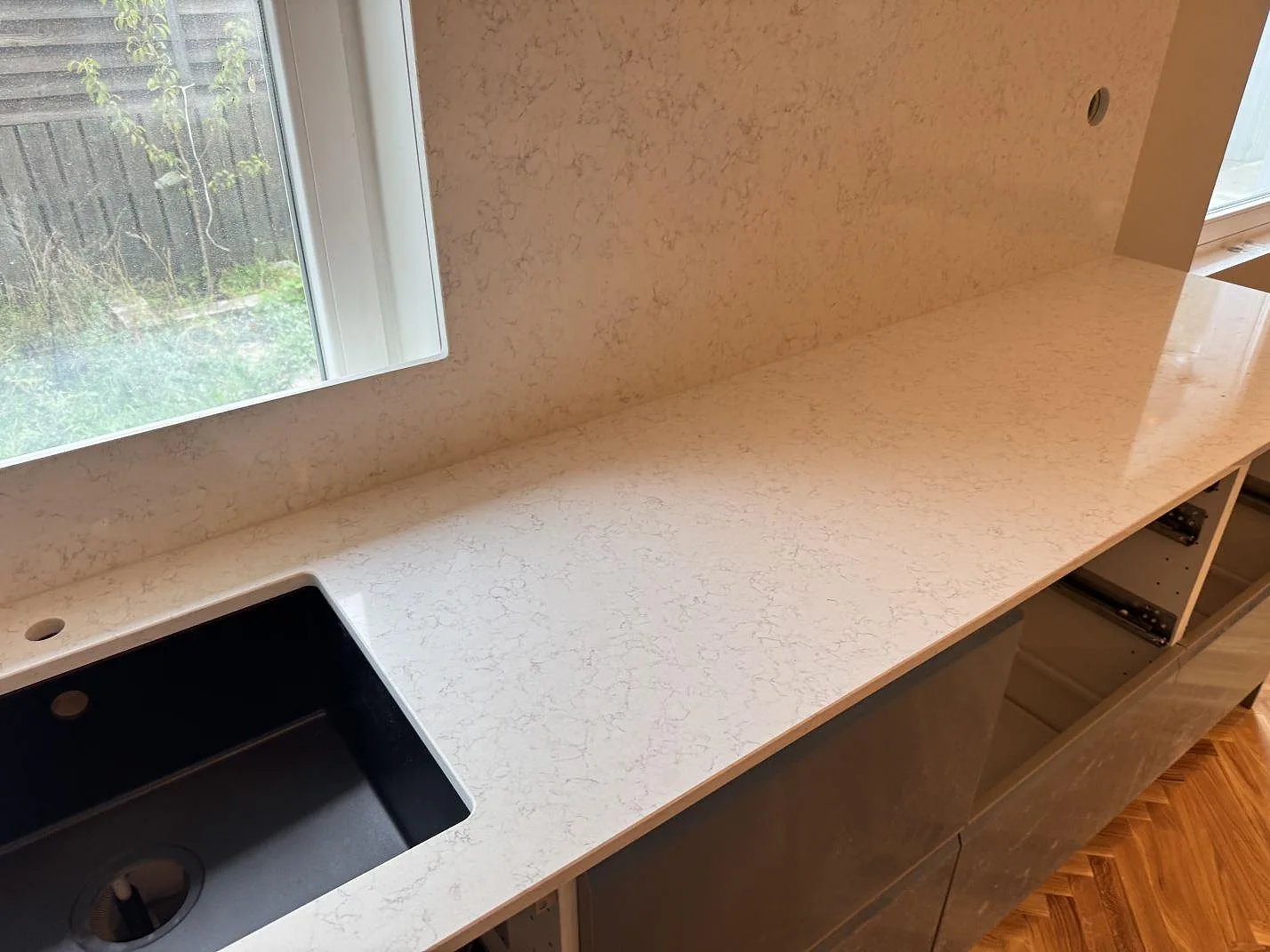 Lång köksbänkskiva i polerad Technistone Noble Arco med svart diskho och sten på väggen i ett kök i Oxie.