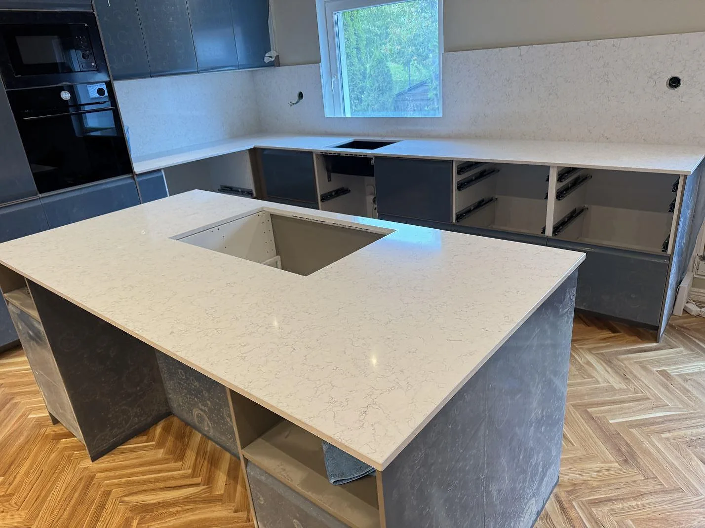 Kök i Oxie med köksö och bänkskivor i polerad Technistone Noble Arco, ljus kvartskomposit med grå teckning.
