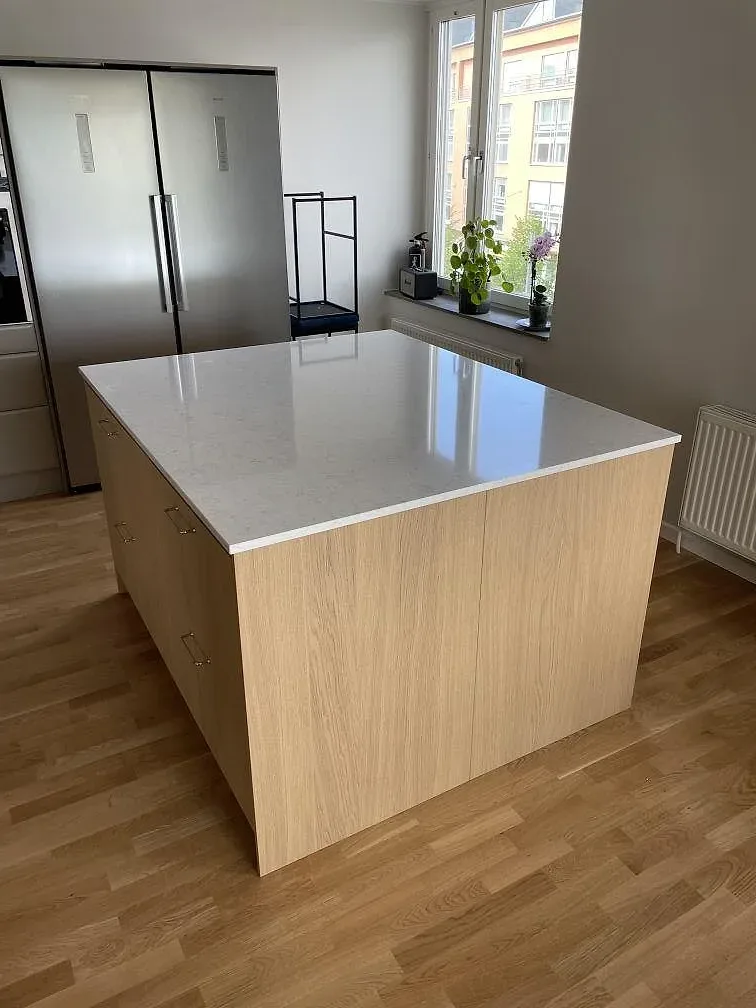 Polerad kompositskiva i Technistone Noble Arco på köksö med ljus träfront och fönsterljus i Stockholm.