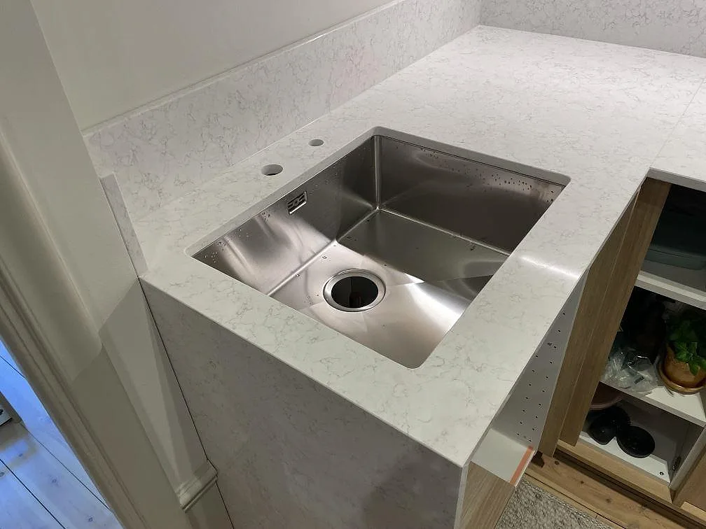 Närbild av polerad Technistone Noble Arco bänkskiva i komposit med rostfri diskho och ljus grå ådring i Stockholm.
