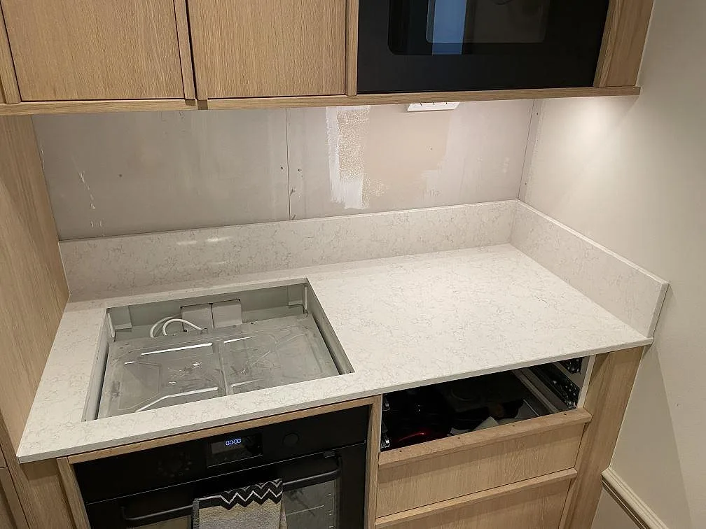 Polerad köksbänkskiva i Technistone Noble Arco komposit med stänkkant och hällurtag under montering i Stockholm.