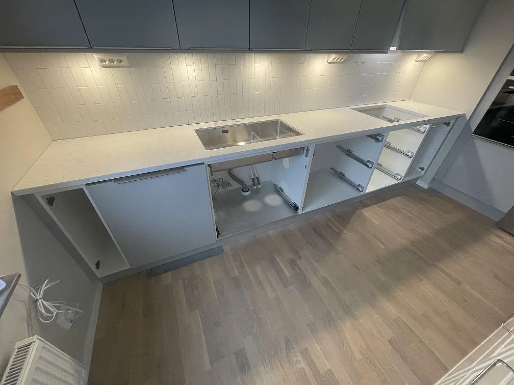 Lång rak köksbänkskiva i Technistone Noble Arco med diskho och urtag för häll, grå överskåp och vit stående kakel i ett kök i Sundbyberg.