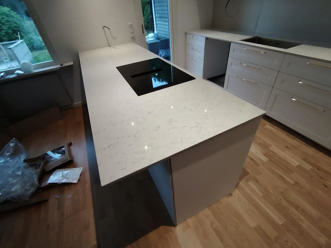 Köksö med bänkskiva i vit polerad Technistone Noble Carrara, häll och lång väggbänk i ett kök i Åkersberga.