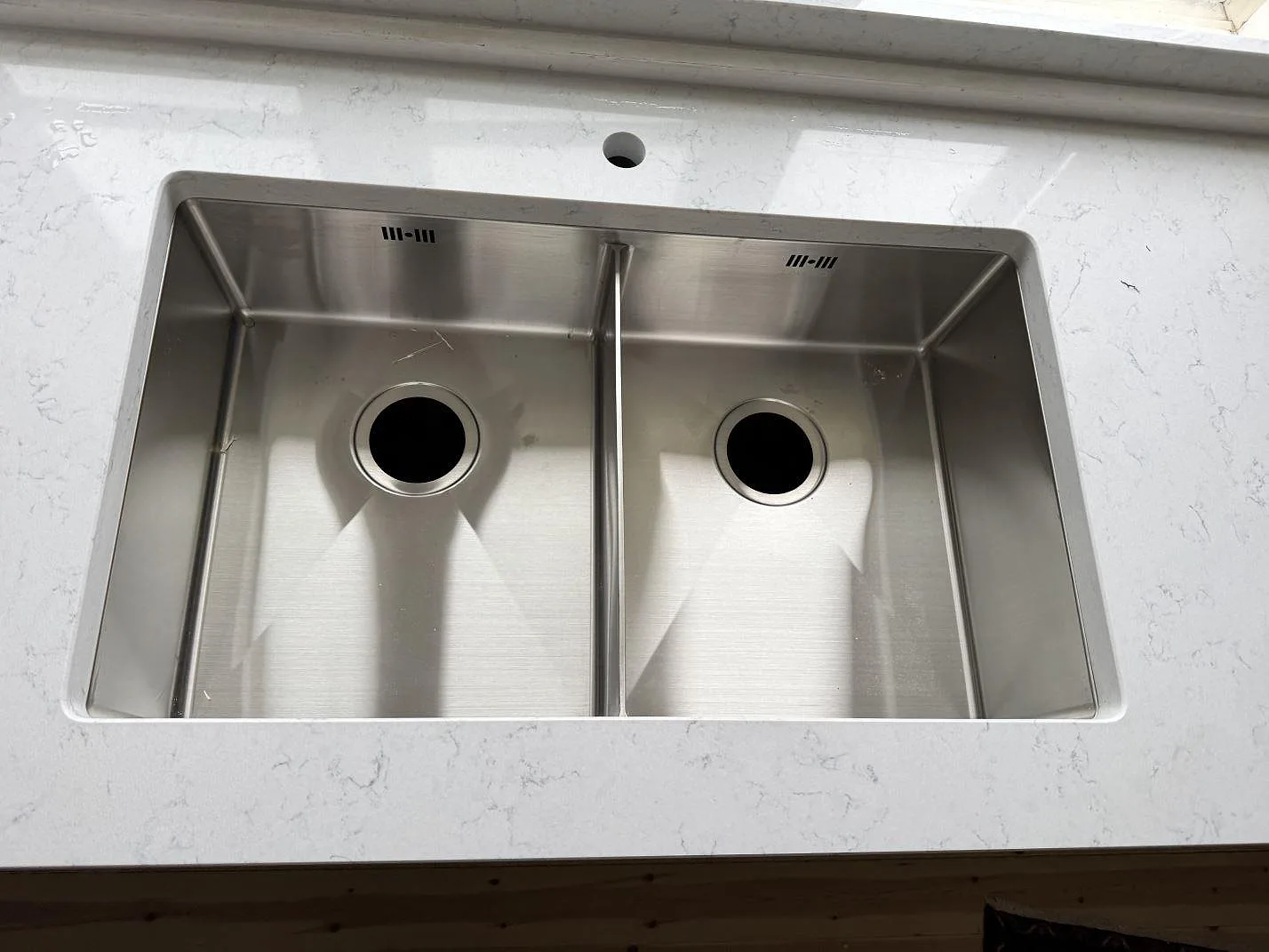Närbild på rostfri dubbelho i polerad Technistone Noble Carrara med grå ådring i Båstad.